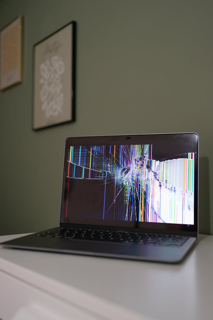 A laptop with a cracked and malfunctioning screen displayed on a desk indoors.